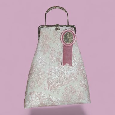 Bolso de mano blanco con detalles rosados y un pin decorativo en una superficie rosa.