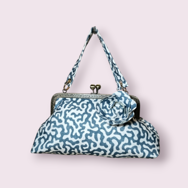 Bolso de mano con diseño azul sobre fondo blanco y cierre metálico.