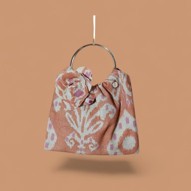 Bolso pequeño de tela con diseño en tonos rosa y anillo metálico.